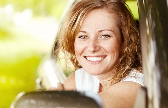 Smiling lady in a car with Spring backdrop.